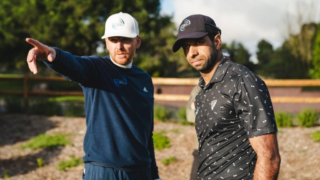 Aaron Rai, on the right, stands attentively as coach, Piers Ward, points in the distance, providing guidance during a golf training session.